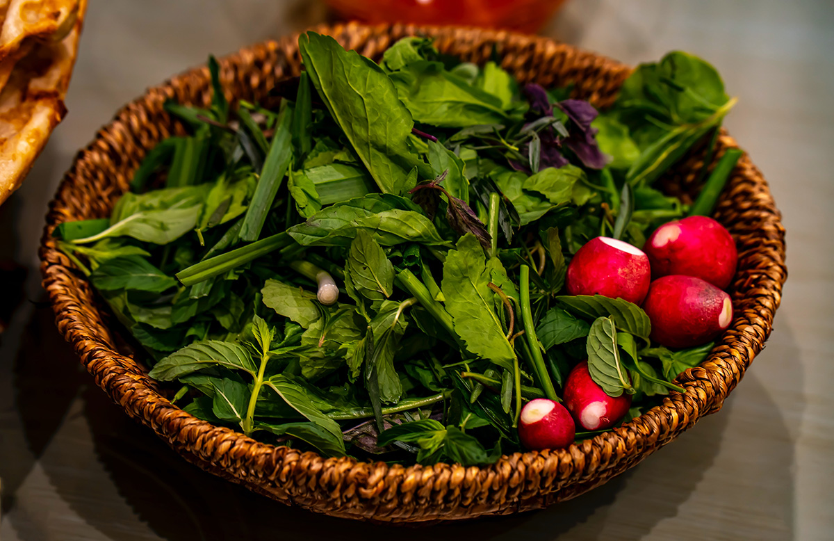 A basket of fresh herbs and radishes.