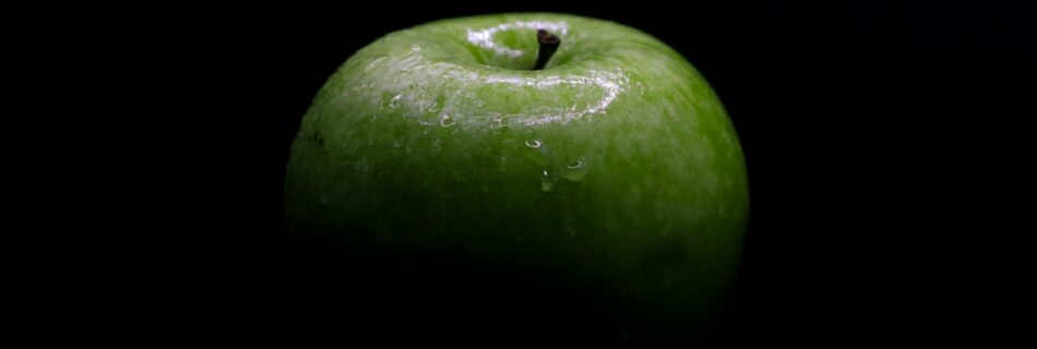 Single apple in the dark with top highlighted in dew